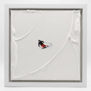 May include: A square white frame containing a textured white canvas with thick, swirled paint strokes. In the center, a small figure of a skier wearing a black jacket, red pants, and a helmet is depicted in motion, carving through the white paint.
