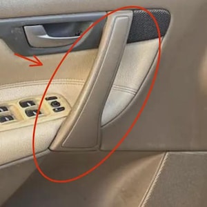 Può includere: Maniglia della portiera dell'auto beige con una copertura per altoparlanti in rete nera. La maniglia è realizzata in un materiale liscio e di colore chiaro ed è integrata nel pannello della portiera dell'auto. Il pannello della portiera presenta anche pulsanti di controllo dei finestrini.