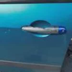 Può includere: Una maniglia per porta auto argentata e blu è montata su una portiera di auto blu acqua. La maniglia ha una forma ovale orizzontale con un accento blu all'estremità. La portiera ha una finitura liscia e lucida.