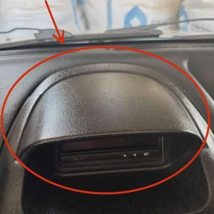 Może przedstawiać: Zbliżenie czarnego elementu deski rozdzielczej z zagłębionym obszarem. Element ma teksturowaną powierzchnię i mały wyświetlacz z literami "H M SET". Deska rozdzielcza znajduje się w pojeździe.