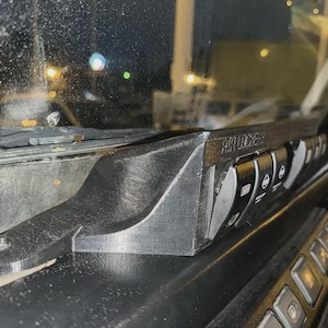 Può includere: Pannello interruttori automobilistico in plastica nera con la scritta "AIR LOCKERS" e diversi interruttori neri con icone bianche. Il pannello è montato su un cruscotto vicino al parabrezza.