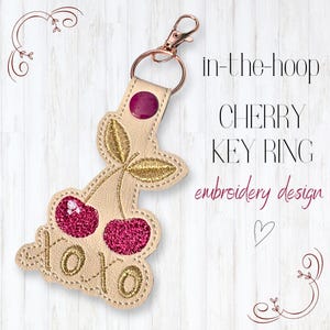 May include: A beige cherry key ring with gold embroidered leaves and two red glitter cherries. The key ring has a gold clasp and a purple button. The text "xoxo" is embroidered on the key ring. The text "in-the-hoop CHERRY KEY RING embroidery design" is also visible.