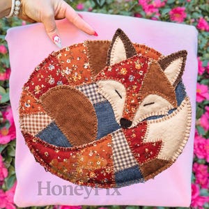 May include: A pink pillow featuring a patchwork fox design. The fox is composed of various fabrics in shades of brown, red, and blue, with a cream-colored face and ears. The text "Honeyfix" is printed at the bottom.