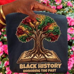May include: A navy blue sweatshirt featuring a detailed tree design with red, yellow, and green leaves, rooted in an open book. The text "BLACK HISTORY HONORING THE PAST" is printed in gold below the tree illustration.