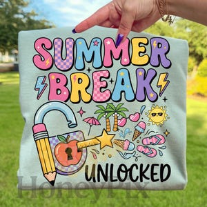 May include: A pale blue t-shirt featuring the text "SUMMER BREAK UNLOCKED" in vibrant, bubble-style lettering. The design incorporates summer-themed illustrations such as palm trees, ice cream, and flip-flops.