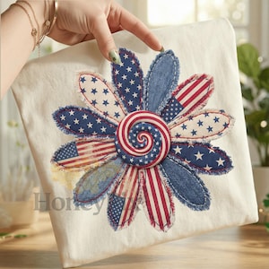 Puede incluir: Un cuadrado de tela blanca con un gran diseño de flor aplicada. Los pétalos de la flor están hechos de mezclilla y tela con patrones de bandera estadounidense y estrellas. El centro de la flor tiene un diseño en espiral en rojo, blanco y azul. La palabra "Honey" es visible en la esquina inferior izquierda.