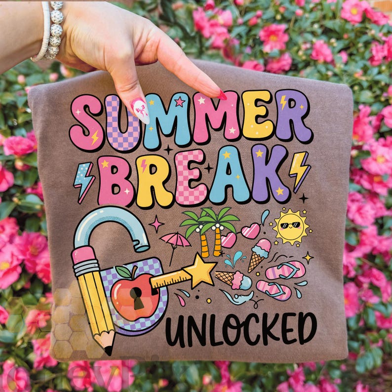May include: A brown t-shirt featuring the text "SUMMER BREAK UNLOCKED" in a vibrant, retro font. The design incorporates a padlock with a pencil key, an apple, and summer icons such as ice cream, sunglasses, and palm trees.