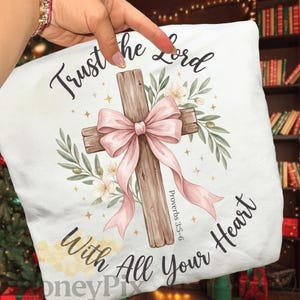 May include: White cushion featuring a cross design. The cross is wooden, decorated with a pink bow and floral details. The text reads "Trust the Lord with All Your Heart" in script.