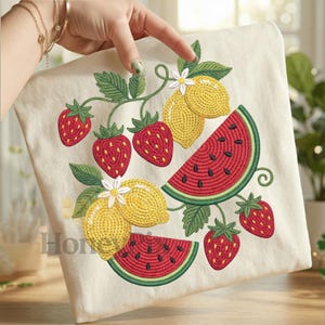 May include: Cream-colored fabric with an embroidered design of strawberries, lemons, and watermelon slices. The fruits are in red, yellow, and green, with black seeds on the watermelon. The design includes green leaves and white flowers.