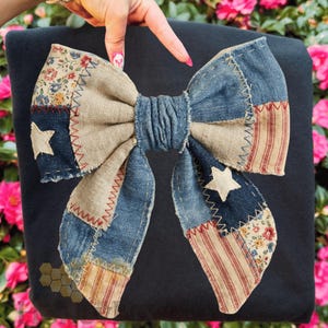 May include: A large, decorative bow with a patchwork design. The bow features denim, floral, and striped fabric patches, with white star accents. The bow is set against a dark background, and the edges are stitched with red thread.