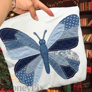 Peut inclure: Un coussin blanc orné d'un grand papillon. Le papillon est composé de différentes nuances de denim bleu, avec des motifs unis, à pois et floraux. Les ailes sont cousues ensemble, créant un effet patchwork.