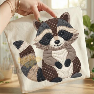 Può includere: Un oggetto in tessuto beige con un design di procione patchwork. Il procione ha una combinazione di colori marrone e grigio con accenti neri. La coda ha un motivo a strisce. La parola "Honey" è visibile nell'angolo in basso a sinistra.