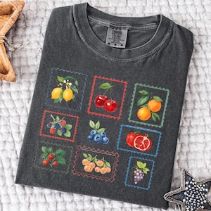 K&ouml;nnte beinhalten: Dunkelgraues Comfort Colors T-Shirt mit farbenfrohem Obststempel-Design. Die Stempel zeigen Zitronen, Kirschen, Orangen, Brombeeren, Blaubeeren, Erdbeeren, Pfirsiche, Granat&auml;pfel und Trauben. Das Shirt hat einen Rundhalsausschnitt und kurze &Auml;rmel.