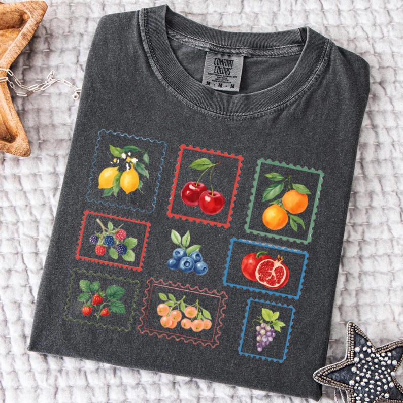 K&ouml;nnte beinhalten: Dunkelgraues Comfort Colors T-Shirt mit farbenfrohem Obststempel-Design. Die Stempel zeigen Zitronen, Kirschen, Orangen, Brombeeren, Blaubeeren, Erdbeeren, Pfirsiche, Granat&auml;pfel und Trauben. Das Shirt hat einen Rundhalsausschnitt und kurze &Auml;rmel.