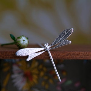 silver dragonfly pendant with wings textured with leaf print. pendant is attached to a silver chain.