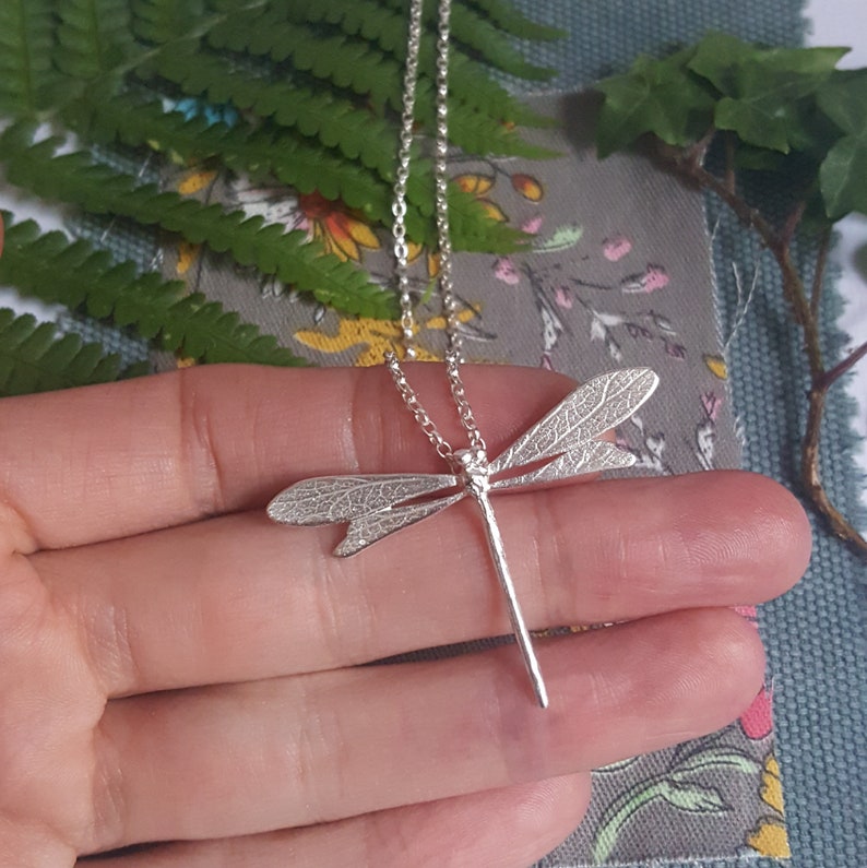 silver dragonfly pendant on a belcher chain rests on a model's hand