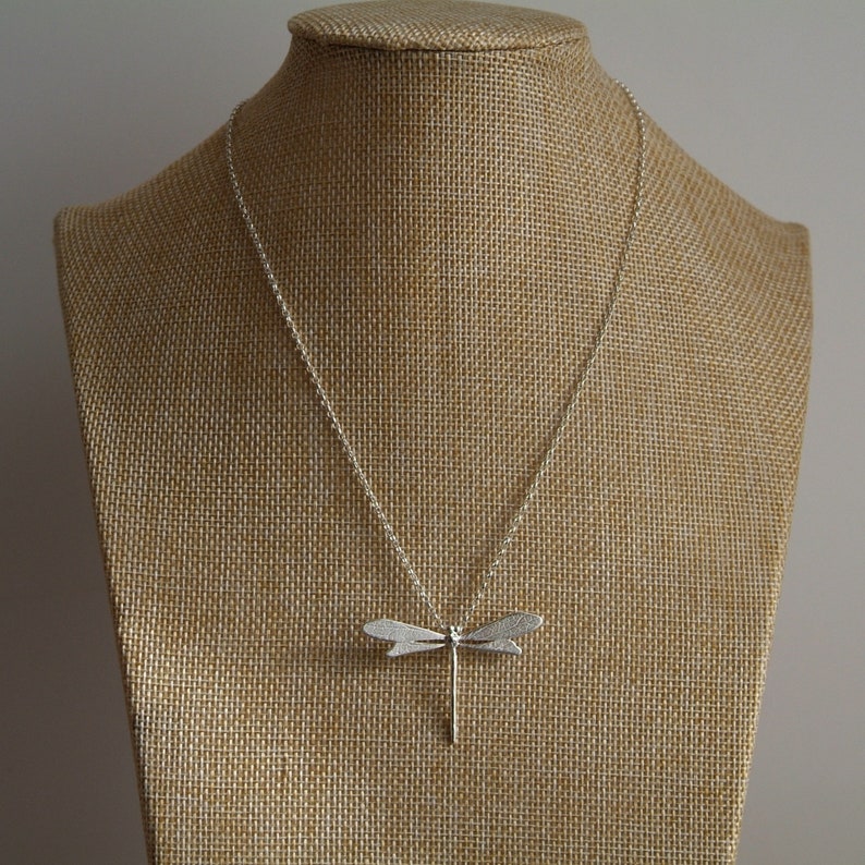 silver dragonfly pendant with chain attached in centre at top, dispplayed on a hessian jewellery bust.