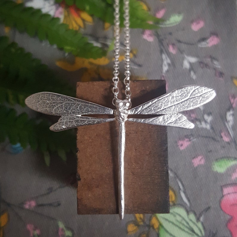 silver dragonfly necklace with chain lies on a floral print background.