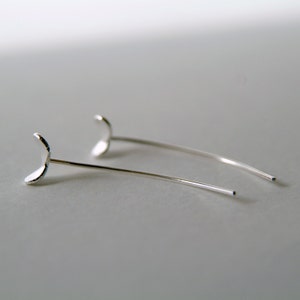 May include: A pair of silver crescent moon earrings with thin, delicate wires.
