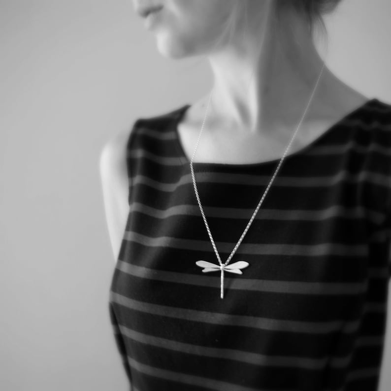 Dragonfly necklace made from silver is worn by a model and hangs long on a chain