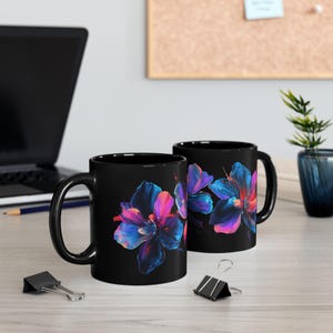May include: Two black ceramic mugs with a floral design. The flowers are painted in shades of blue, pink, and purple on a black background.