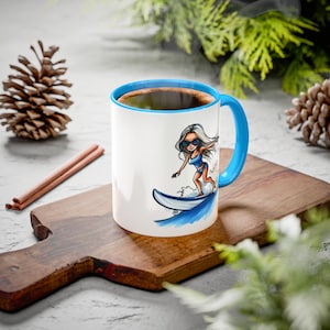 May include: White ceramic mug with a blue rim and handle. The mug features a cartoon illustration of a woman in a swimsuit riding a surfboard on a wave.