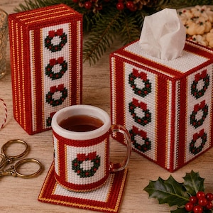 May include: A plastic canvas set featuring a tall rectangular box, a square tissue box cover, a mug cozy, and a square coaster. Each piece is crafted with red and white grid patterns, gold metallic accents, and embroidered Christmas wreath motifs.
