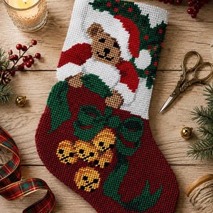 May include: A needlepoint Christmas stocking featuring a brown teddy bear wearing a red and white Santa hat. The lower section is deep red with a green ribbon design and four yellow jingle bells. The background is white with green holly leaves.