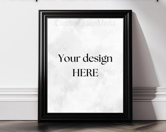 May include: A black picture frame mockup with a white background and the text "Your design HERE" inside the frame. The frame is on a white wall with a wooden floor.