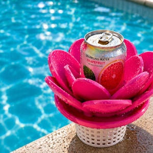 Op de afbeelding: Een felroze, bloemvormige drijvende drankhouder met een blikje grapefruit bruiswater. De drankhouder bevindt zich in een zwembad, met het water op de achtergrond. Het blikje is zilverkleurig met de tekst "Sparkling Water Grapefruit".