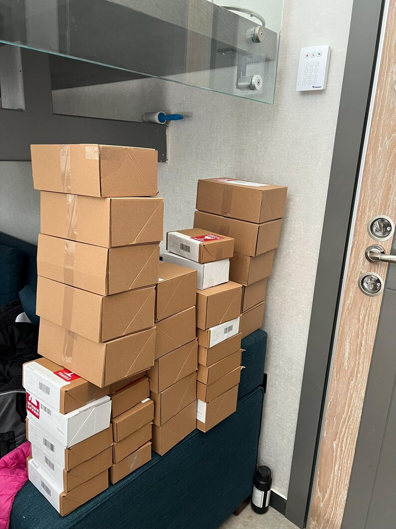 Puede incluir: Una pila de cajas de cart&oacute;n de varios tama&ntilde;os, algunas con etiquetas blancas y rojas, apiladas sobre un banco tapizado de color turquesa. Las cajas sugieren una variedad de art&iacute;culos.