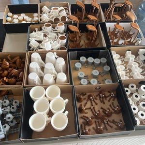 Puede incluir: Variedad de peque&ntilde;os objetos impresos en 3D en varias etapas de finalizaci&oacute;n, organizados en cajas de cart&oacute;n. Los art&iacute;culos incluyen tazas, formas abstractas y otras piezas decorativas en blanco, marr&oacute;n y gris.