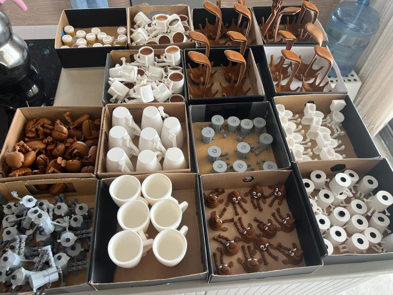 Puede incluir: Variedad de peque&ntilde;os objetos impresos en 3D en varias etapas de finalizaci&oacute;n, organizados en cajas de cart&oacute;n. Los art&iacute;culos incluyen tazas, formas abstractas y otras piezas decorativas en blanco, marr&oacute;n y gris.