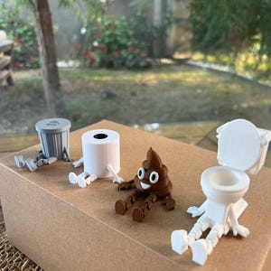 Puede incluir: Colecci&oacute;n de figuras caprichosas impresas en 3D, que incluyen un cubo de basura gris, un rollo de papel higi&eacute;nico blanco, un emoji de caca marr&oacute;n sonriente y un inodoro blanco. Cada figura tiene piernas y brazos adjuntos.