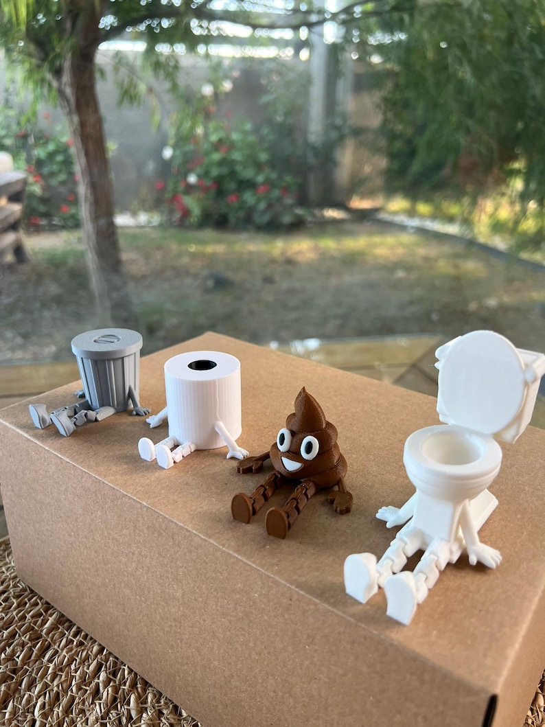 Puede incluir: Colecci&oacute;n de figuras caprichosas impresas en 3D, que incluyen un cubo de basura gris, un rollo de papel higi&eacute;nico blanco, un emoji de caca marr&oacute;n sonriente y un inodoro blanco. Cada figura tiene piernas y brazos adjuntos.