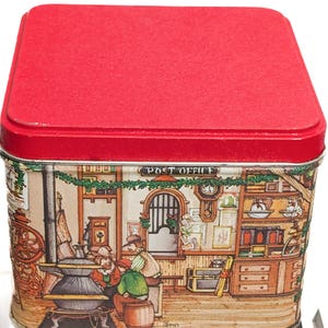 Puede incluir: Una lata rectangular con tapa roja y una detallada ilustración de una escena de oficina de correos. La ilustración presenta personas, una estufa y las palabras "Post Office" encima de la escena. La lata es probablemente para almacenamiento o fines decorativos.