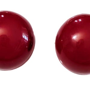 Puede incluir: Dos esferas redondas y brillantes, de color rojo oscuro, posiblemente cuentas o elementos decorativos, se muestran sobre un fondo blanco. Las esferas tienen una superficie lisa y reflectante, con reflejos que sugieren un acabado pulido.