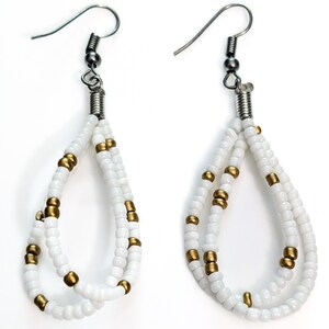May include: A pair of white beaded earrings with a teardrop design. The earrings feature small white beads and gold-colored accents. The ear wires are silver-colored. The earrings are displayed against a white background.