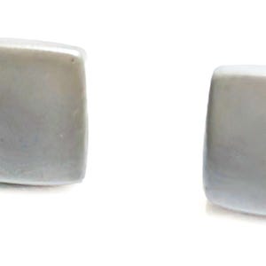 May include: Two square, light gray cufflinks with rounded corners are displayed against a white background. The cufflinks have a smooth, polished appearance, suggesting a formal accessory.
