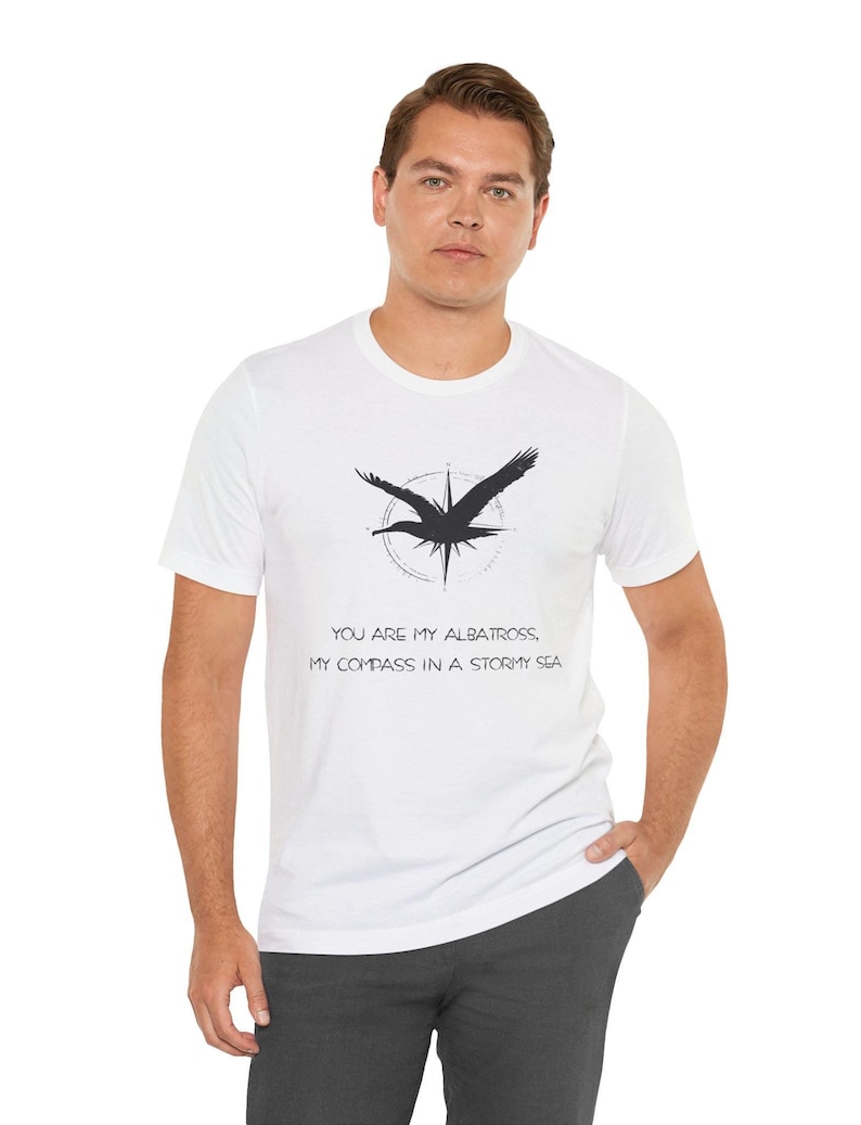 May include: White t-shirt with a black silhouette of an albatross flying over a compass. The text "You are my albatross, my compass in a stormy sea" is printed on the shirt.
