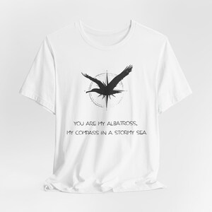 May include: White t-shirt with a black albatross graphic and compass design. The text "You are my albatross, my compass in a stormy sea" is printed below the graphic.