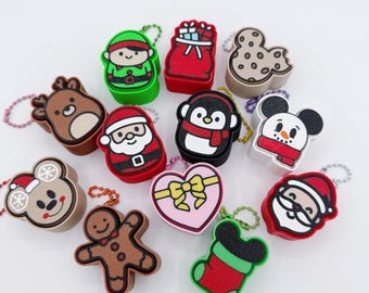 May include: A collection of Christmas-themed keychains in various shapes, including Santa, reindeer, and gingerbread men. The keychains are colorful and feature cartoon-like designs. The word "clicker" is written in a playful font above the keychains.