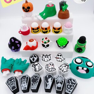 Puede incluir: Una colección de figuras en miniatura con temática de Halloween. El surtido incluye una calabaza, un pie cortado, una lápida, caramelos de maíz, globos oculares, fantasmas, ataúdes y una cabeza de zombi. Las figuras son de varios colores.