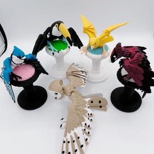 May include: A selection of bird figurines, including a blue jay, toucan, owl, and others. Each bird is mounted on a decorative stand with a black base. The birds have detailed designs and vibrant colours.