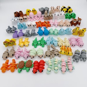 May include: A collection of colorful, miniature animal figurines, including ducks, octopuses, bears, and turtles. The figurines are made of a smooth material and are arranged on a white surface. The collection features a variety of colors and designs.