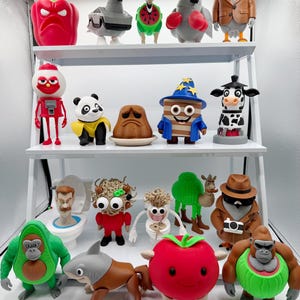 May include: A collection of whimsical figurines displayed on white shelves. The figurines include a red pepper, a pigeon, a giraffe with a watermelon slice, a boxing pigeon, a bird in a blazer, a robot, a panda, a sad-faced dessert, a cake wizard, and a cow.