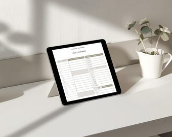 May include: A digital tablet displaying a daily planner layout. The tablet is black with a white screen, resting on a white surface. A small white pitcher with decorative flowers and a small pink bowl are also on the surface.