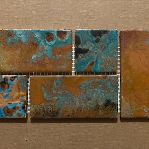 May include: A close-up of a mosaic tile sheet featuring a blend of blue, green, and brown hues. The tiles are laid out in a staggered pattern, resulting in a distinctive and eye-catching design.