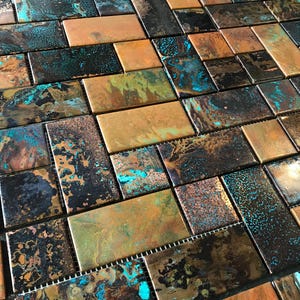 Può includere: Un motivo a mosaico di piastrelle con piastrelle rettangolari in varie tonalità di rame, bronzo e verde acqua. Le piastrelle hanno un aspetto invecchiato e usurato, con trame screziate e variazioni di colore. L'effetto complessivo è un mix di estetica industriale e naturale.