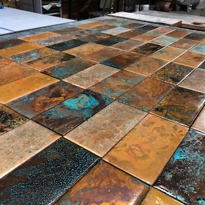 Peut inclure: Une grille de carreaux rectangulaires présentant une finition en cuivre vieilli avec un mélange de brun métallique, de bronze et de patine vert turquoise oxydé. Chaque carreau affiche une texture de surface unique et mouchetée.